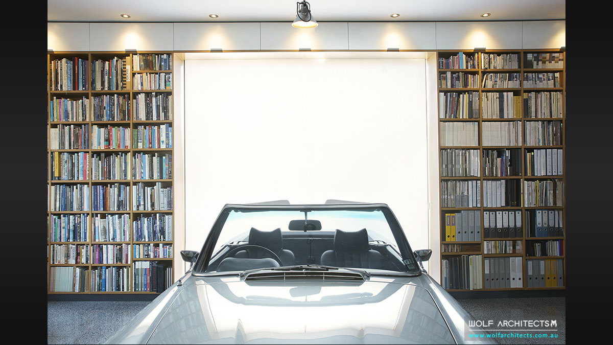 Wall of books with car in modern architects house by Wolf Architects